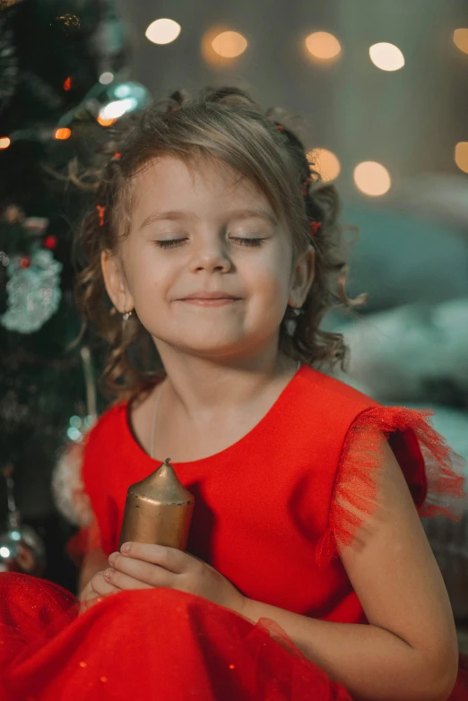 a  sits by the christmas tree holding a gold bell