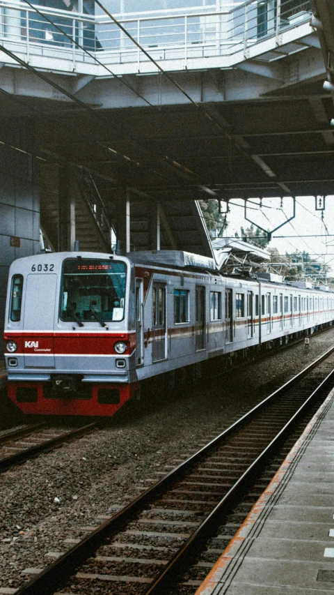a red and white train pulling into a train station, a colorized photo, unsplash, sōsaku hanga, south jakarta, grey, 90s photo, 🚿🗝📝