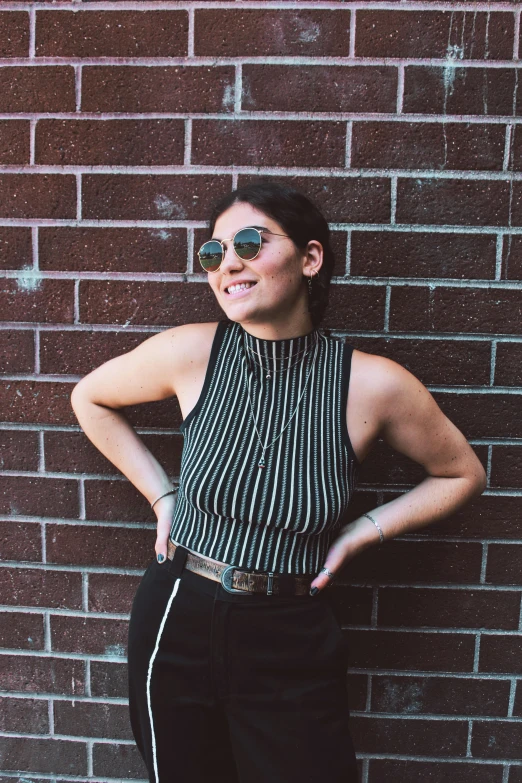 a woman standing in front of a brick wall, inspired by Ion Andreescu, pexels contest winner, wearing a cropped top, striped shirt, black halter top, promotional image