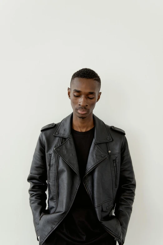 a man standing in front of a white wall, an album cover, inspired by Barthélemy Menn, trending on unsplash, she wears leather jacket, adut akech, androgynous person, profile image