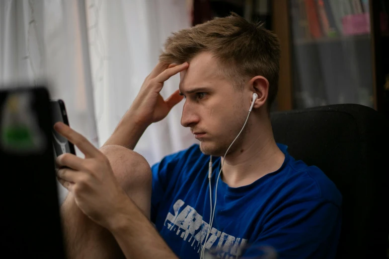 a man sitting in a chair looking at a cell phone, by Adam Marczyński, trending on pexels, realism, headphones on his head, male teenager, pouting, looking at monitor