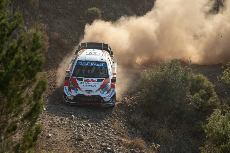 the rally car races through the sand as dust is pouring up behind it