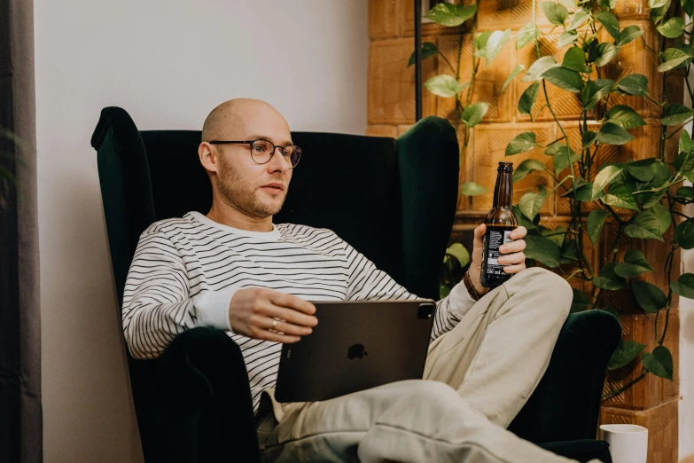 a man holding a beer and tablet while sitting on the couch