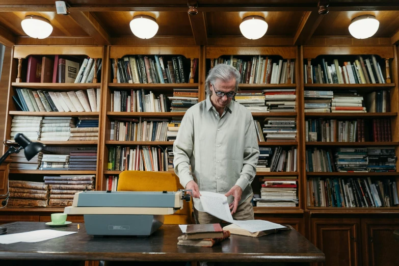 a man standing in front of a laptop in a library, private press, renzo piano, with one vintage book on a table, grey, on vellum