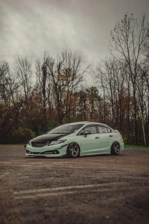 a small light green hatchback parked in a parking lot with the hood up