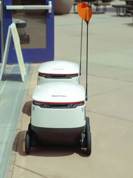 two robots sitting next to each other on a sidewalk, optimus sun orientation, cart, seen from the side, white