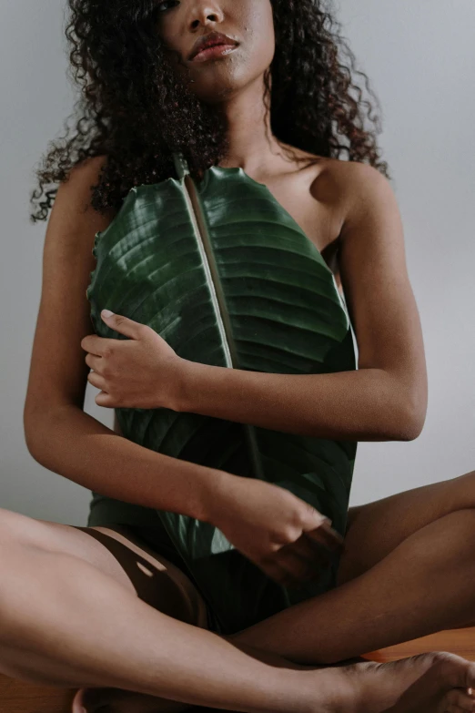 a woman sitting on top of a wooden floor, inspired by Ren Hang, trending on pexels, chest covered with palm leaves, dark brown skin, banana, intimate holding close