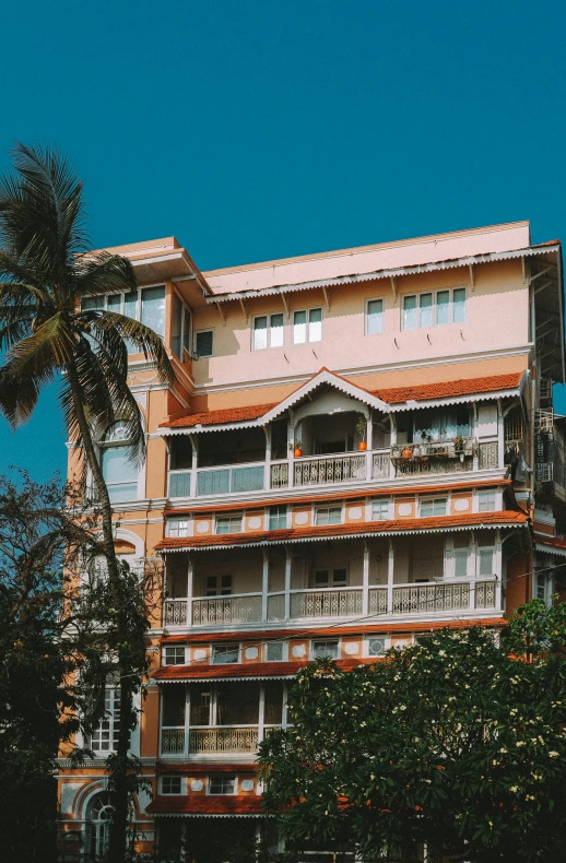 a tall building sitting on top of a lush green field, pexels contest winner, art nouveau, palm trees outside the windows, vastayan, crenellated balconies, near the beach