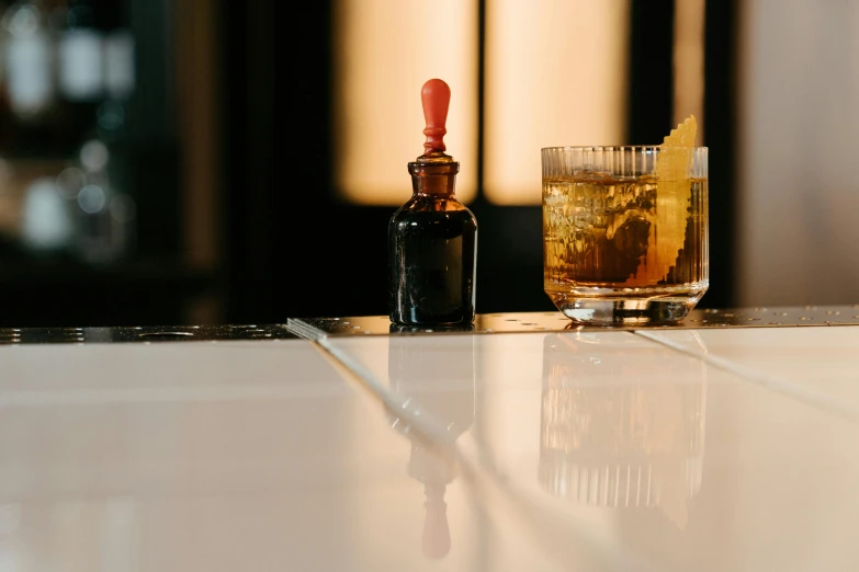 a glass sitting on top of a counter next to a bottle, unsplash, renaissance, screwdrivers, lacquered, taking tobacco snuff, profile image