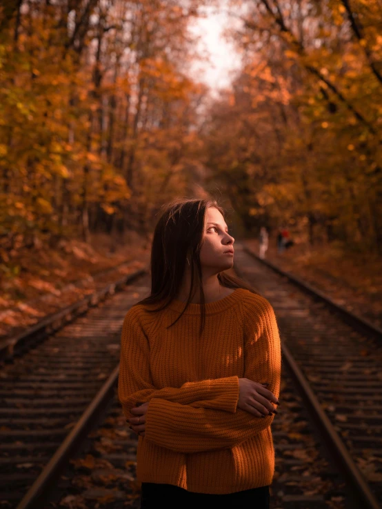 a woman standing in the middle of a train track, inspired by Elsa Bleda, pexels contest winner, realism, autumn color, thoughtful ), orange hue, low quality photo