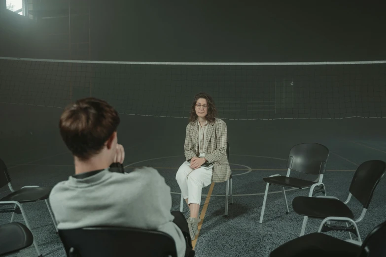 a woman sitting on top of a chair in a room, dark people discussing, sports setting, mental health, in the center of the image
