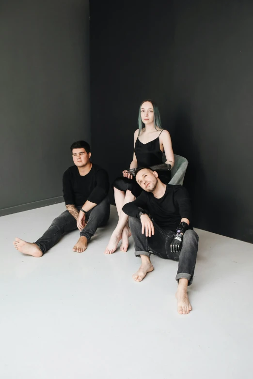 a group of people sitting on top of a white floor, pale skin, with a black background, trio, standing in corner of room