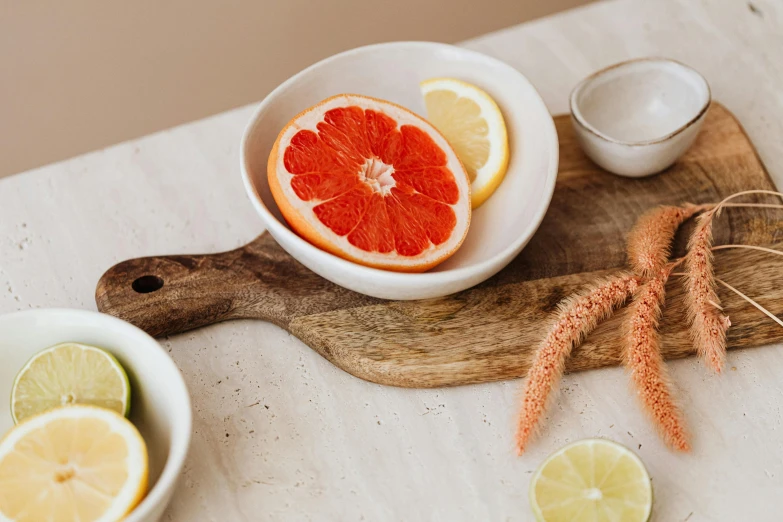 a wooden cutting board topped with slices of grapefruit, a still life, trending on pexels, organic ceramic white, bowl filled with food, subtle detailing, intimate holding close