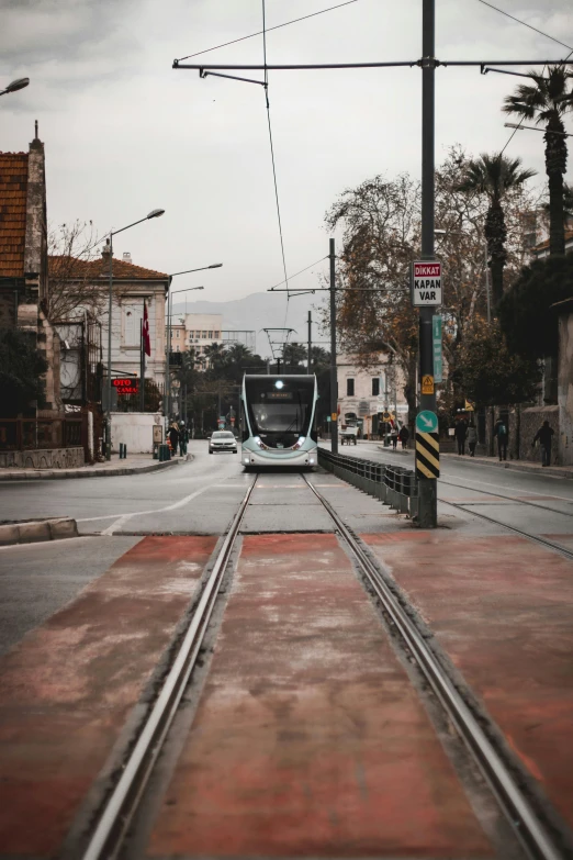 a train traveling down a street next to tall buildings, a picture, pexels contest winner, greece, tram, grayish, paved roads