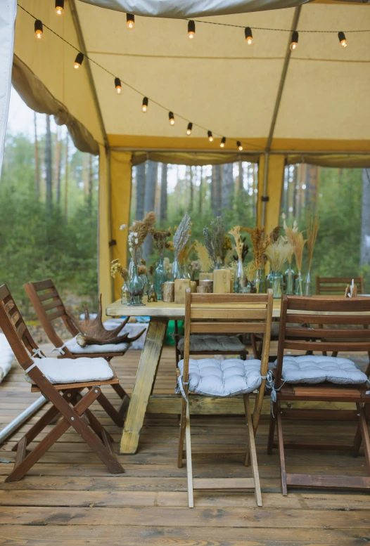 a group of wooden chairs sitting on top of a wooden floor, tents, dining table, boreal forest, marquee