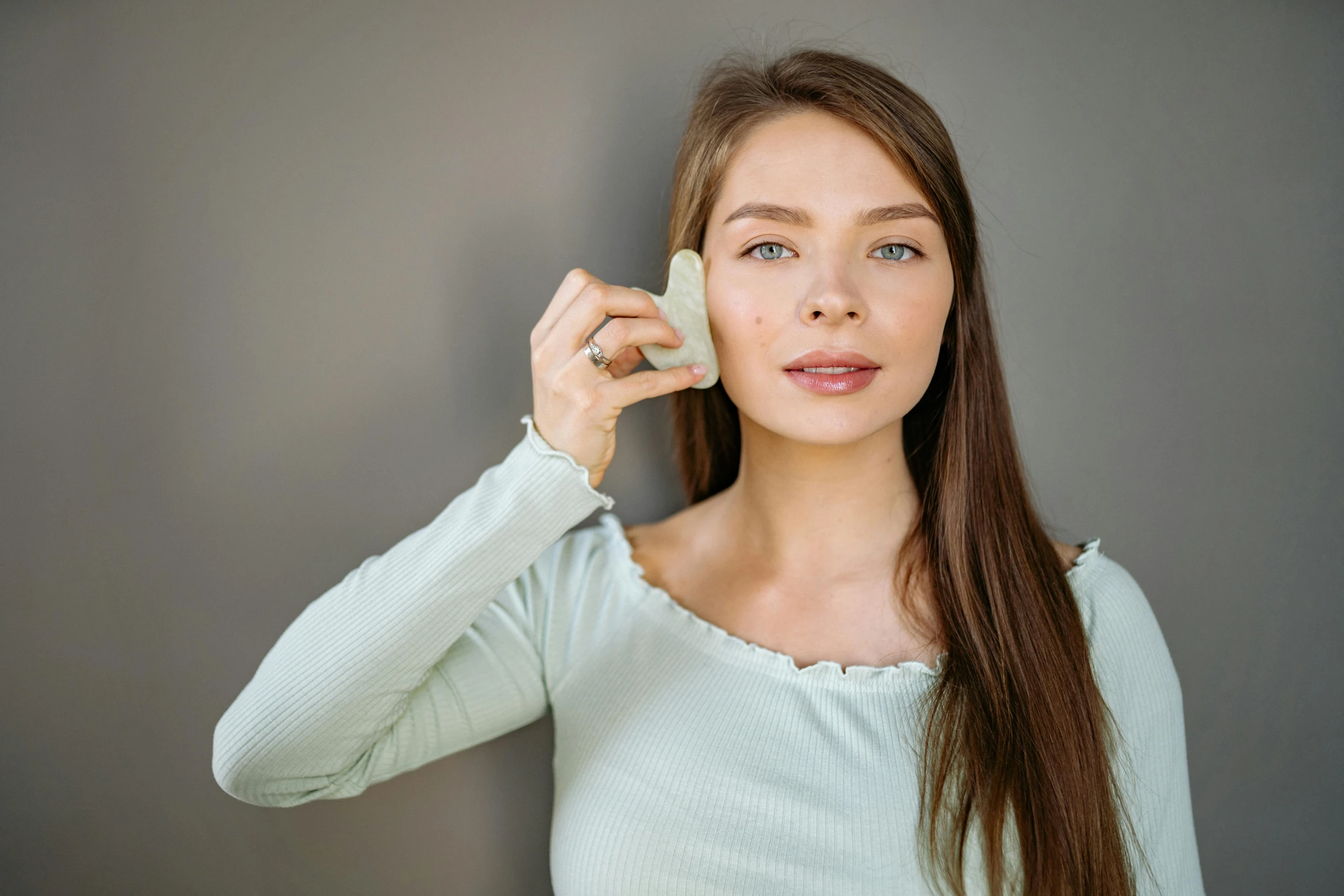 a woman holding a cell phone to her ear, trending on pexels, art nouveau, beauty mark on cheek, on grey background, silicone skin, pale green glow