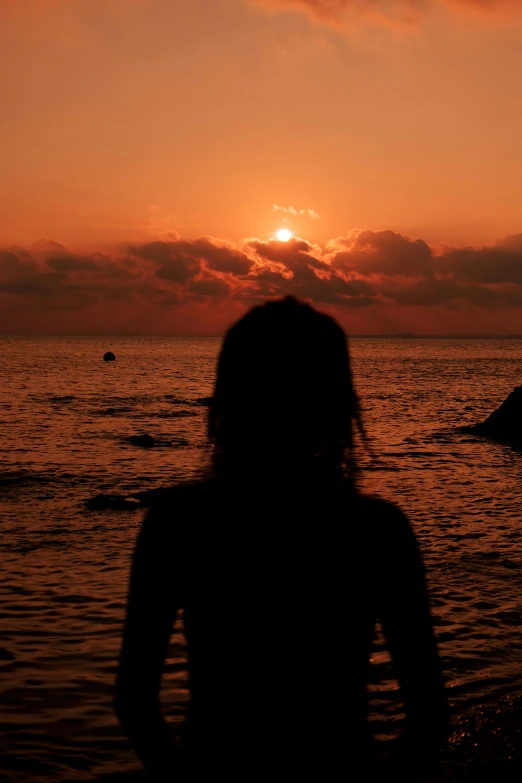 a woman standing on top of a beach next to the ocean, orange sun set, profile image, sunset kanagawa prefecture, silhouette :7