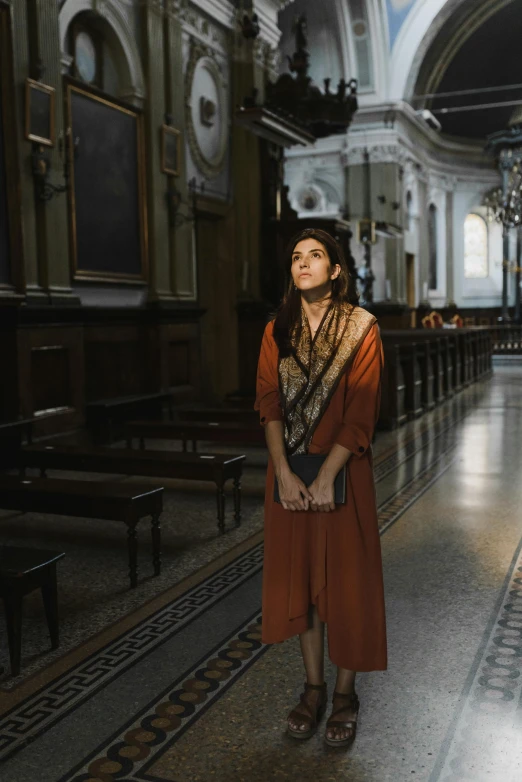 a woman in a red dress standing in a church, inspired by Modest Urgell, trending on unsplash, renaissance, wearing brown robes, 8 k movie still, shohreh aghdashloo, street photo