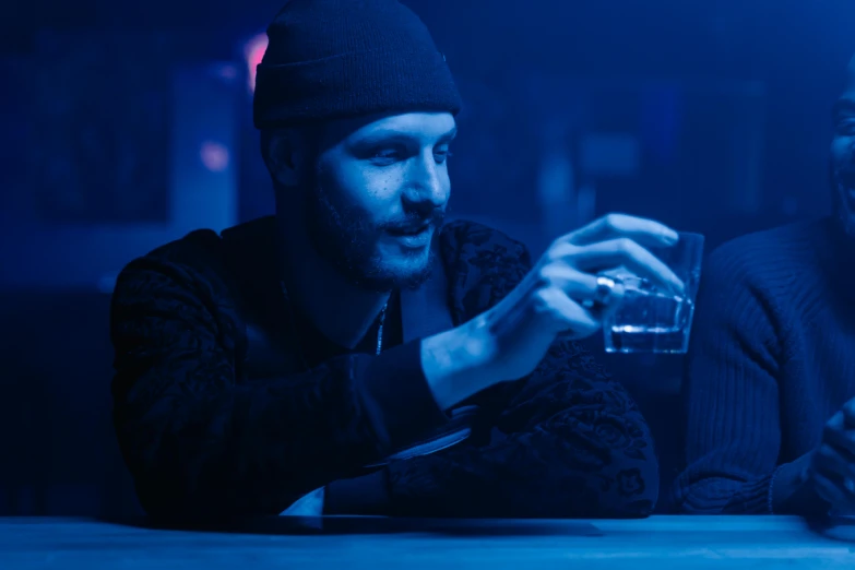a couple of men sitting next to each other at a table, a hologram, inspired by Elsa Bleda, trending on pexels, drinking whiskey, demna gvasalia, blue mood, [ theatrical ]