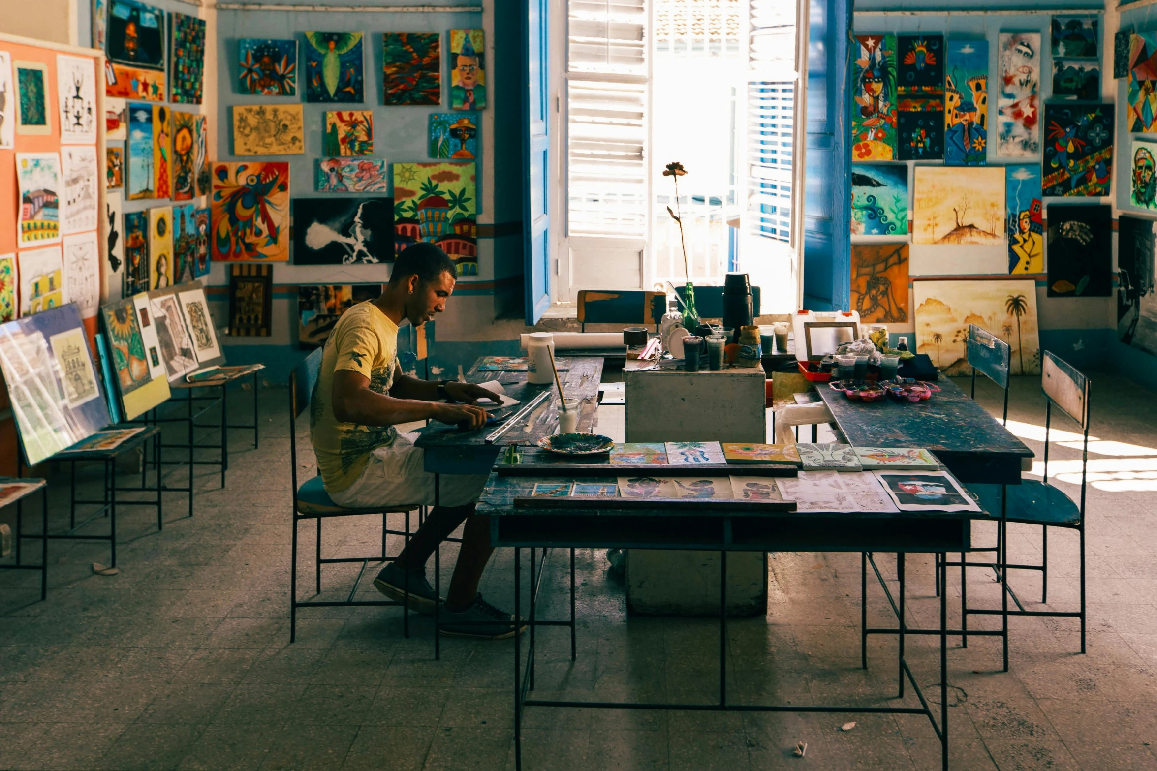 a man sitting at a table working on a laptop, a cubist painting, pexels contest winner, bengal school of art, cuba, beautiful creative space behind, 🎨🖌️, crafts and souvenirs