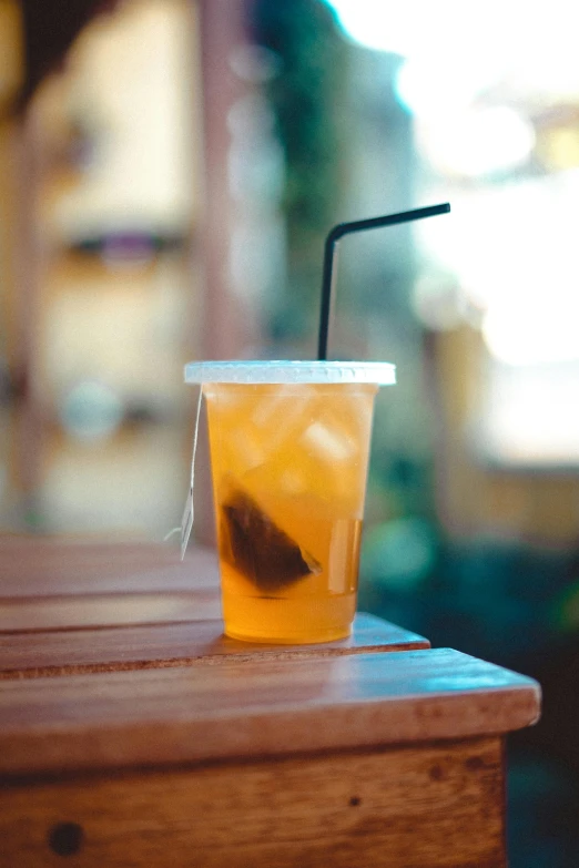 a drink sitting on top of a wooden table, iced tea glass, profile image, straw, square