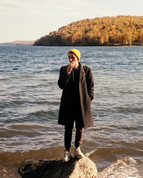 a man standing on top of a rock in the water, androgynous face, in fall, profile image, maple syrup sea