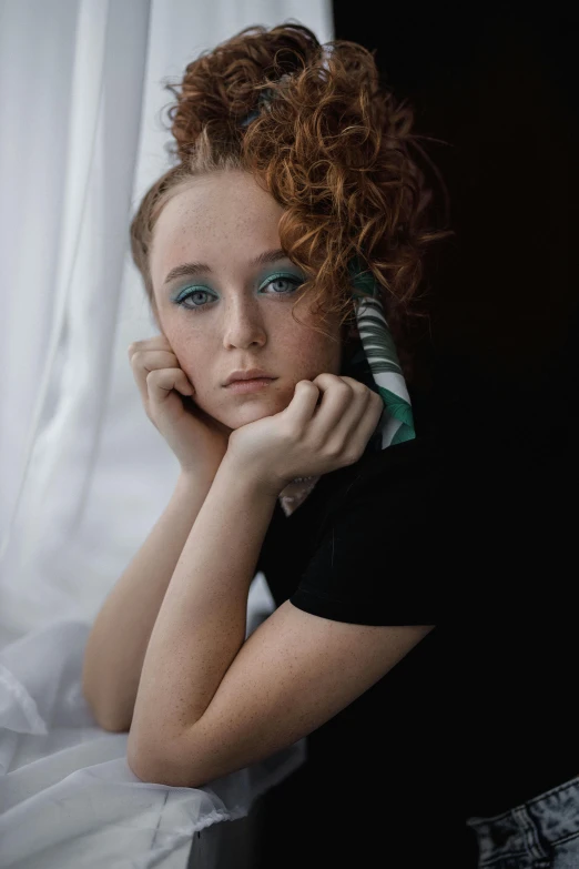 a woman sitting on top of a bed next to a window, a colorized photo, inspired by Nan Goldin, trending on pexels, red curled hair, somber turquoise eyes, portrait of depressed teen, with a black background