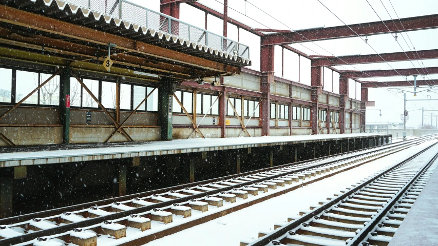 a snow - covered train station that has multiple rows of tracks under the roof