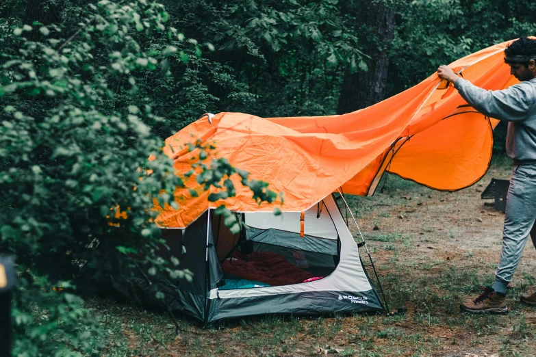 a man is setting up a tent in the woods, by Adam Marczyński, hurufiyya, neon orange, awnings, thumbnail, instagram post