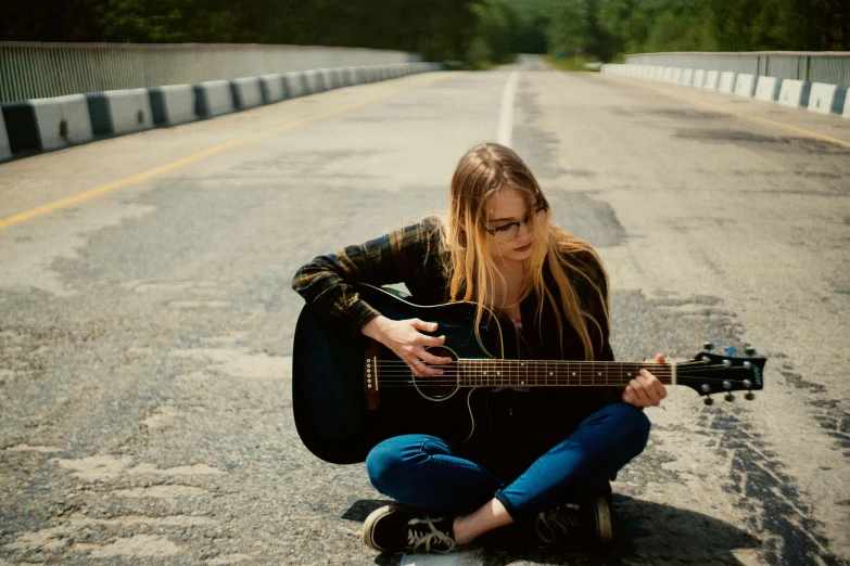 a woman sits on the ground and plays an acoustic guitar