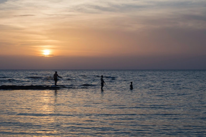 a couple of people that are standing in the water, a picture, unsplash contest winner, sunset beach, people swimming, sparsely populated, family