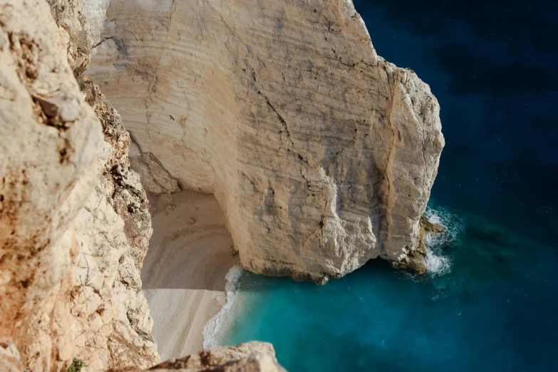 a man standing on top of a cliff next to a body of water, pexels contest winner, greek nose, laying on sand, chalk cliffs above, deep colour