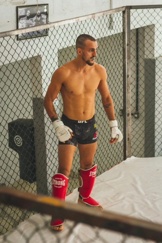 a man wearing knee pads standing in a cage, inspired by Volkan Baga, thiago alcantara, profile image, taken in the early 2020s, wearing red shorts