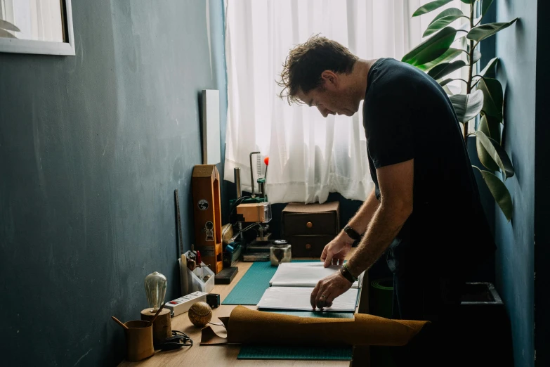 a man that is standing in front of a desk, by Lee Loughridge, pexels contest winner, crafting, holding notebook, lachlan bailey, artisanal art