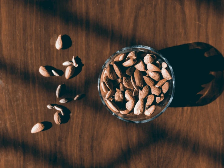 a glass bowl filled with nuts on top of a wooden table, an album cover, by Julia Pishtar, trending on pexels, background image, seeds, a high angle shot, animation