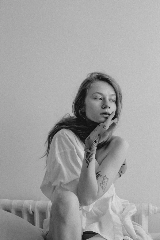 a black and white photo of a woman sitting on a bed, by Hannah Frank, antipodeans, anna dittman, dressed in a white t shirt, tattoos, pastel'