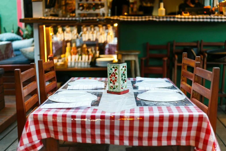 a red and white checkered table cloth sitting on a wooden table with a candle in the middle of the table