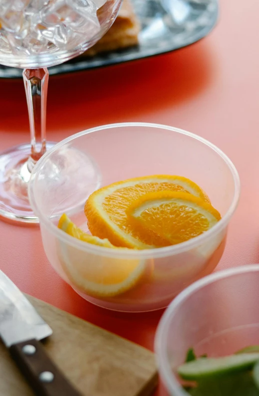 a table topped with a bowl of fruit next to a knife, orange and orange slices, transparent, zoomed in, drinking