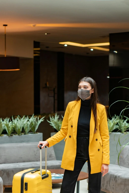 a woman in yellow jacket with mask standing in front of her luggage