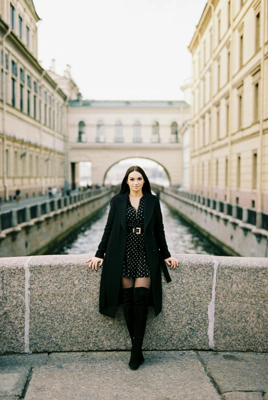 a woman standing on a bridge next to a river, an album cover, by Lucia Peka, pexels contest winner, stockholm city portrait, oona chaplin, in moscow centre, wearing black coat