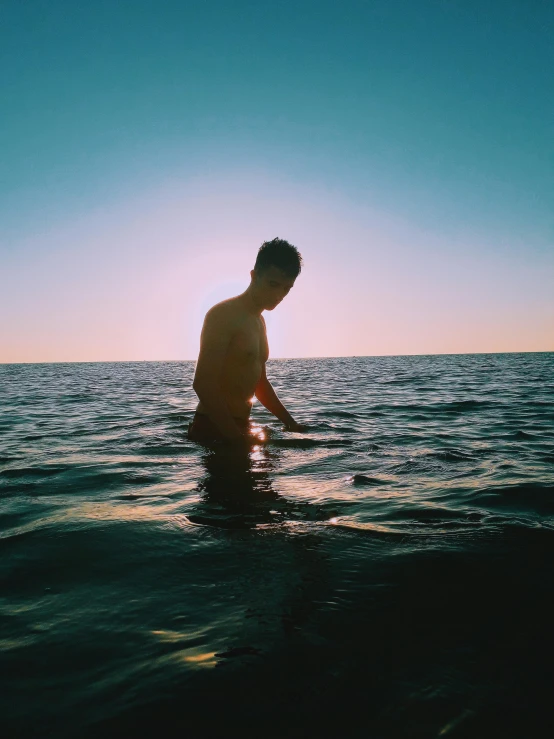 a man standing in the ocean at sunset, unsplash, happening, slightly tanned, declan mckenna, thin young male, subreddit / r / whale