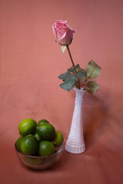 a white vase filled with limes next to a rose