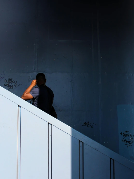 a man walking up a flight of stairs talking on a cell phone, a photo, trending on unsplash, postminimalism, blue wall, with his back turned, taken in the late 2010s, shadowy informant