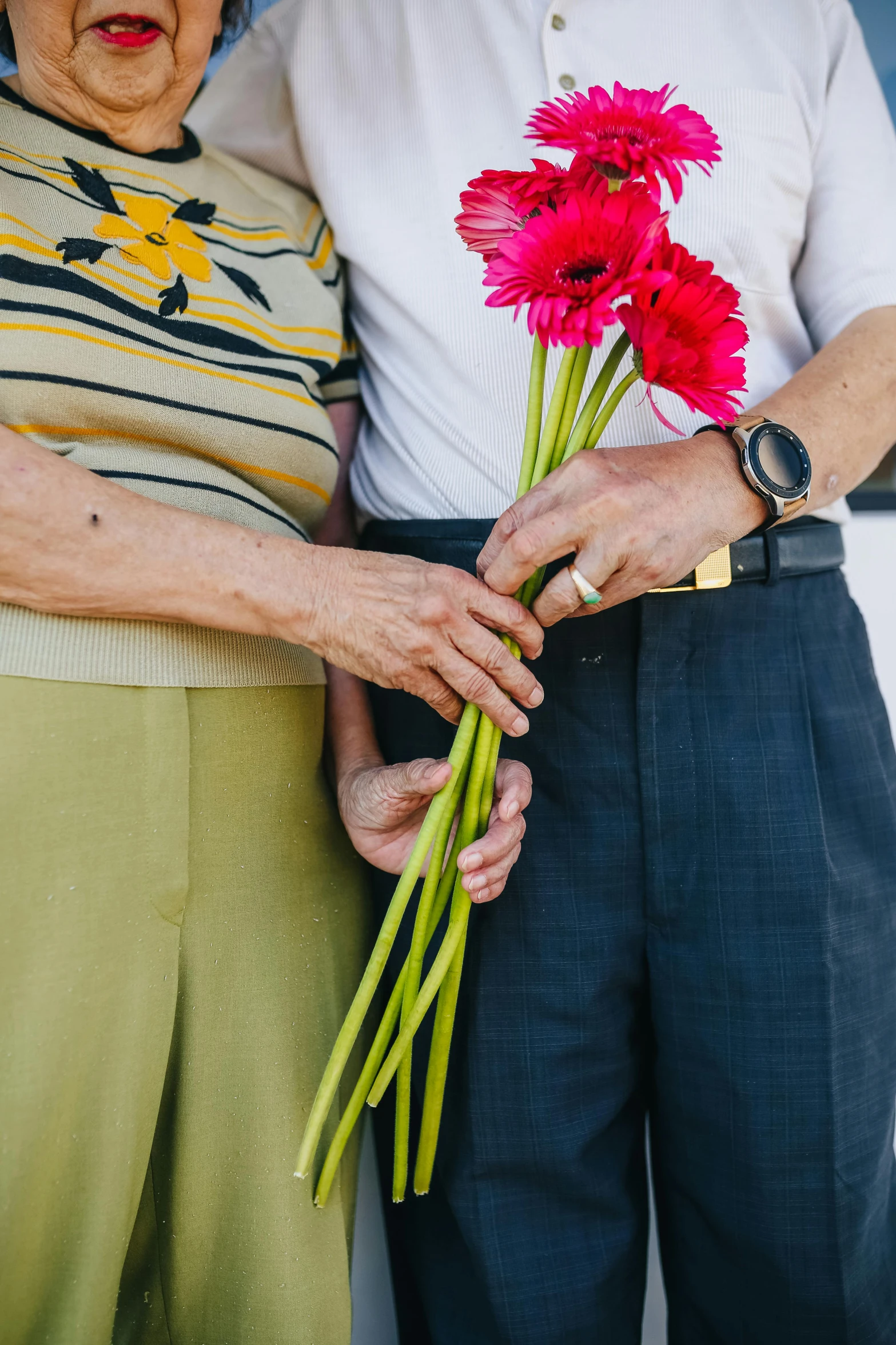 a man and woman standing next to each other holding flowers, by Dan Frazier, unsplash, two old people, lgbtq, embrace, sleek hands