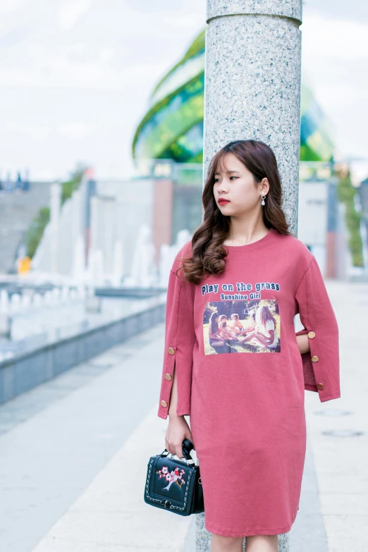 a woman standing next to a column holding a purse, a picture, inspired by Kim Jeong-hui, happening, long sleeves, lalisa manobal, in tshirt, maroon red