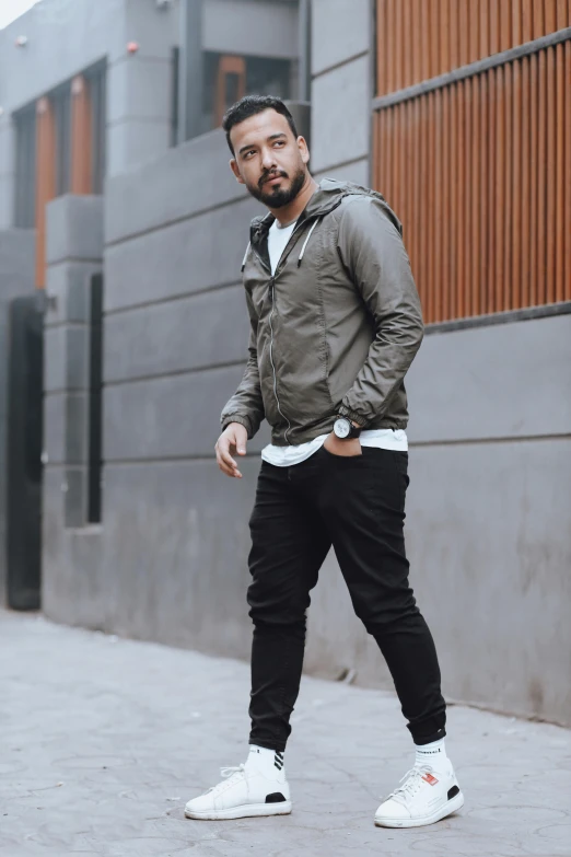a man standing on a sidewalk in front of a building, inspired by Germán Londoño, pexels contest winner, wearing jeans and a black hoodie, grey jacket, wearing military outfit, profile image