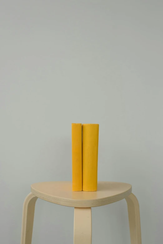 a yellow vase sitting on top of a wooden stool, by Harvey Quaytman, holding books, two organic looking towers, 200 mm, soft rubber