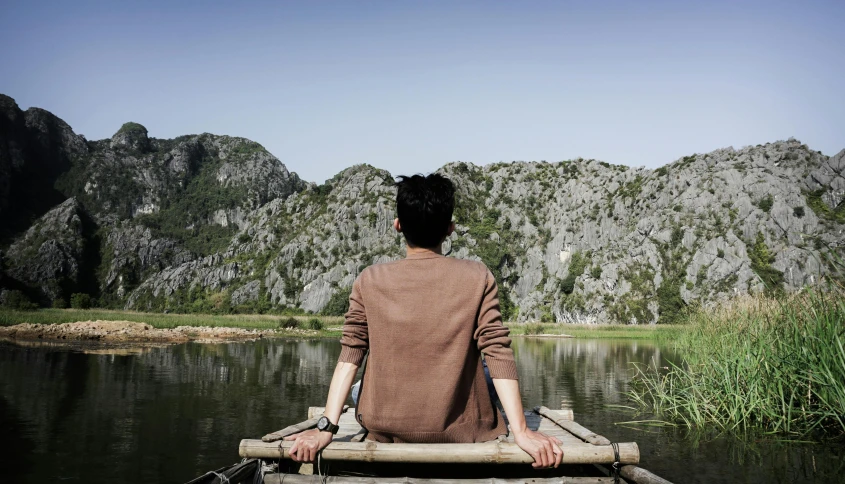 a man sitting in the boat with mountains behind him