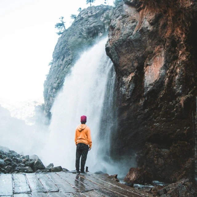 a person in an orange sweater and a waterfall in the background