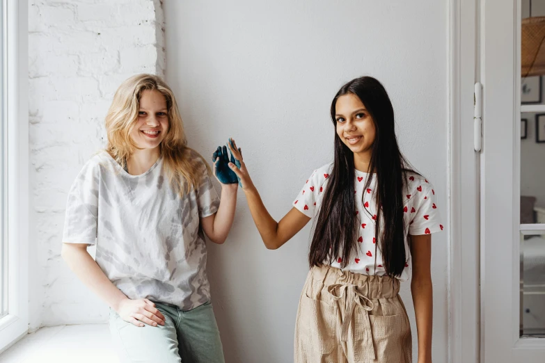 two women standing next to each other near a window, pexels contest winner, wave a hand at the camera, teenagers, 15081959 21121991 01012000 4k, white wall coloured workshop